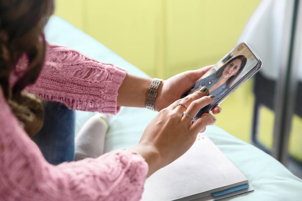 A woman holds up a smart screen where she is talking to a healthcare professional, with a Mayo Clinic logo visible on the screen.