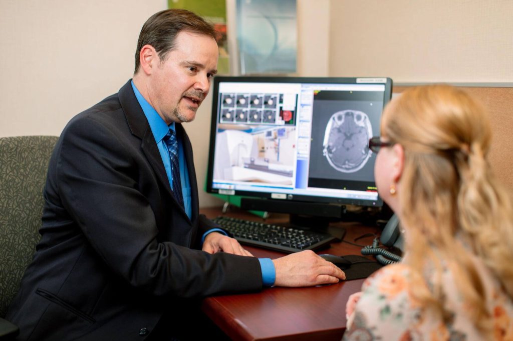 Dr. Paul D. Brown discusses a brain scan displayed on a computer monitor with a patient during a consultation.