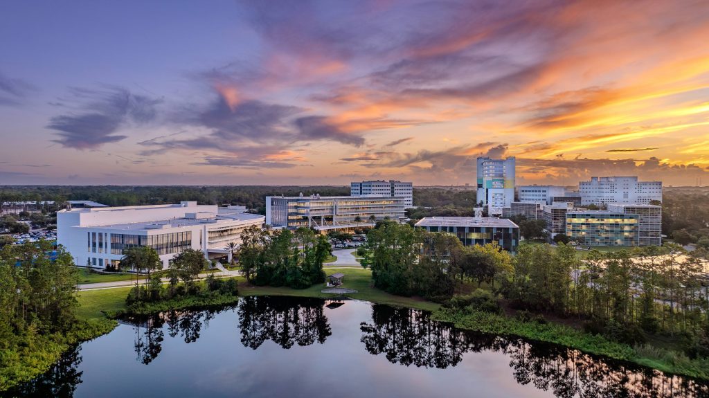 Mayo Clinic in Florida campus at sunset, with hospital buildings surrounded by trees and reflected in a pond.