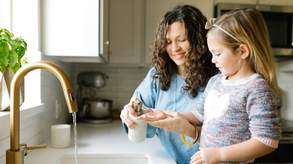 A woman and young girl stand in front of a sink, preparing to wash their hands with soap.