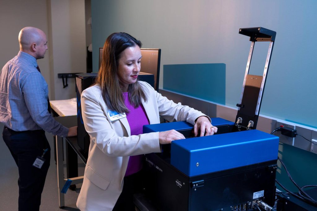Jessica Lancaster, Ph.D., Mayo Clinic immunologist, places a sample into a light-sheet microscope as a colleague works behind her.