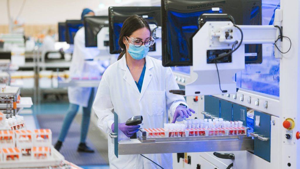 梅奥诊所实验室的一位女性保健研究员在实验室用试管工作时戴着眼镜和PPE，口罩，手套