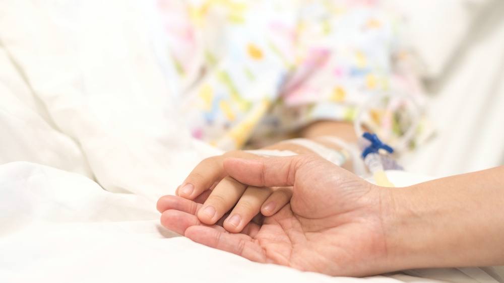 一名静脉输液的儿童患者在医院的床上手牵着手睡觉，一名成人握着她的手为安慰