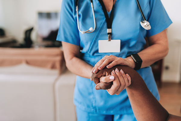 Un profesional de la salud con uniforme azul sostiene suavemente la mano de un paciente en un gesto de apoyo.